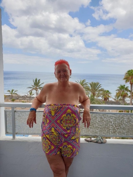 Obese nan with spiky red hair unveils her tits on balcony before posing naked