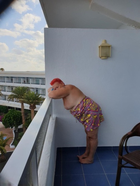 Obese nan with spiky red hair unveils her tits on balcony before posing naked