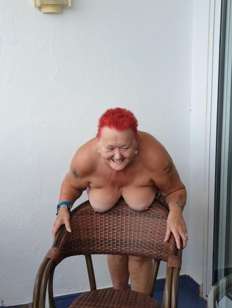 Obese nan with spiky red hair unveils her tits on balcony before posing naked